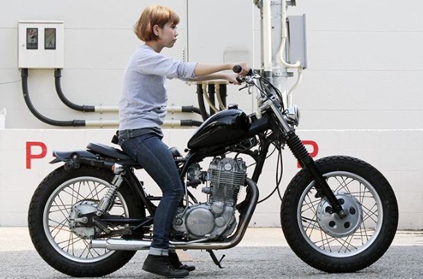 Person sitting on a motorcycle in front of a building with visible branding.