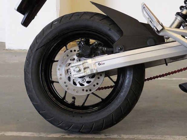 Close-up of a motorcycle wheel with chain on a concrete floor.