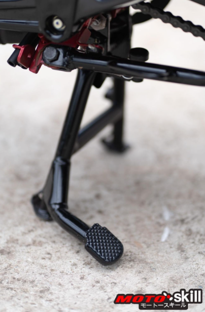 Close-up of a motorcycle foot peg and chain on a textured surface with 'Moto Skill' branding.