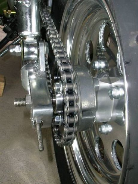 Close-up of a motorcycle chain and sprocket system on a concrete floor.