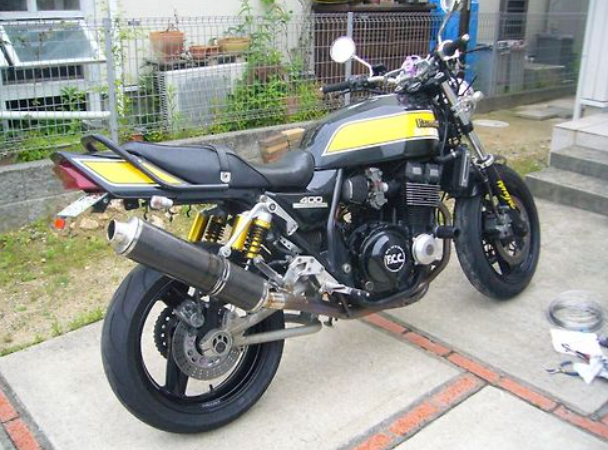 Black and yellow motorcycle parked on a concrete surface with a building and plants in the background.