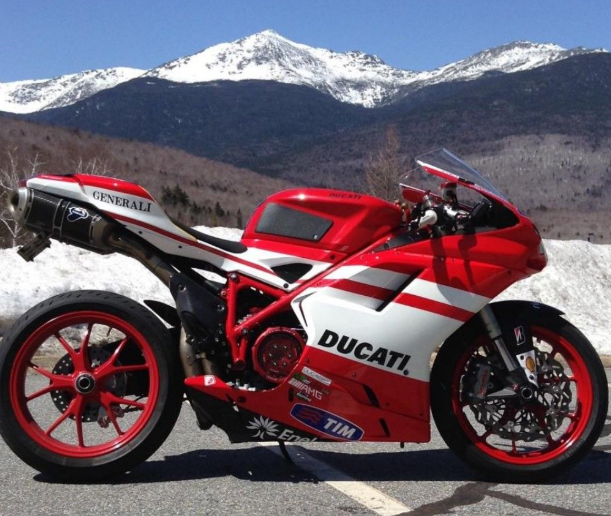 Red and white Ducati motorcycle on a road with mountains in the background