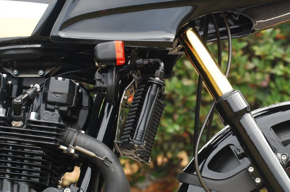 Close-up of a motorcycle's front suspension and brake system with a blurred green background.