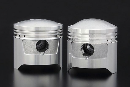 Two metallic piston-like objects on a reflective surface with a dark background