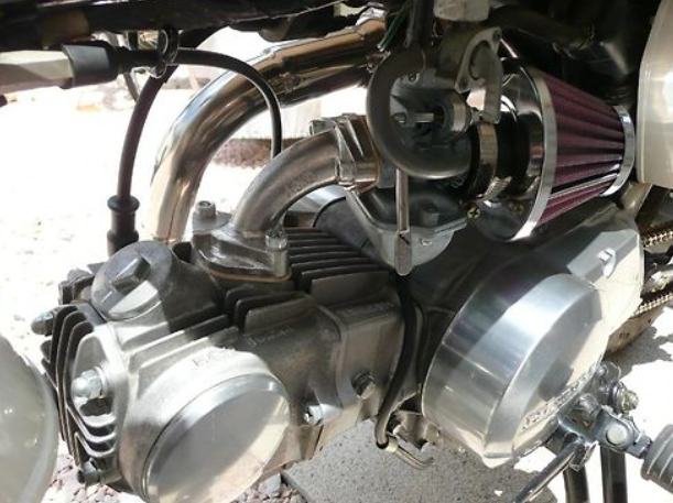 Close-up of a motorcycle engine with visible components on a textured surface.