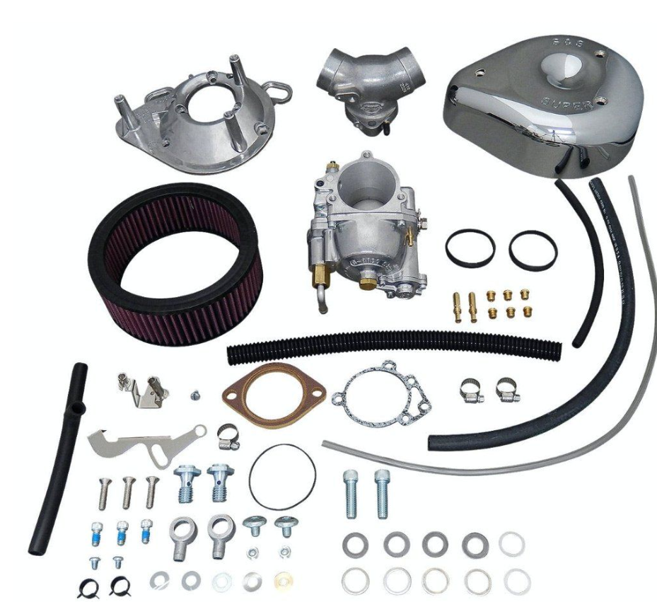 Collection of automotive parts including a carburetor, air filter, and various metal components on a white background.
