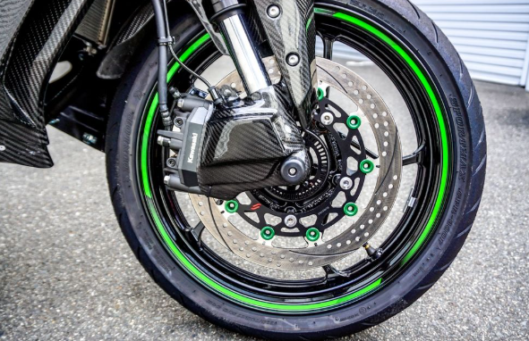 Close-up of a motorcycle wheel with green accents on a pavement background