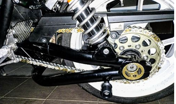 Close-up of a motorcycle chain and sprocket system on a tiled floor.