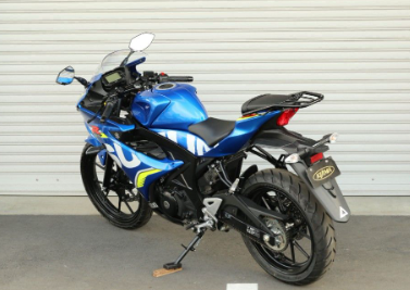Blue motorcycle with black seat and tires on a gray floor against a white wall.