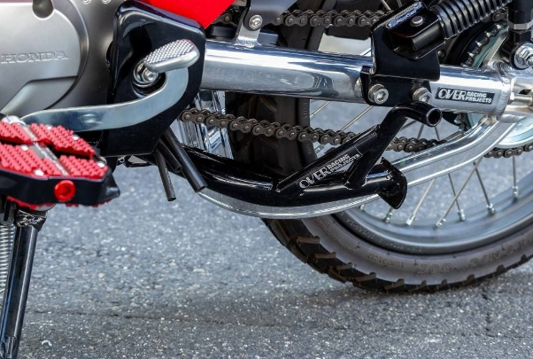Close-up of a motorcycle chain and sprocket with a visible brand logo on a gray surface.